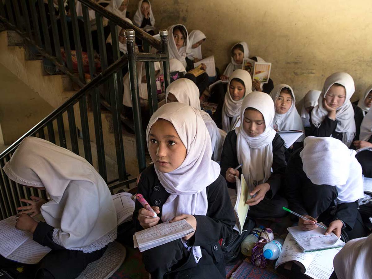 Afghan schoolgirls in white headscarves studying with their notebooks on a crowded school staircase